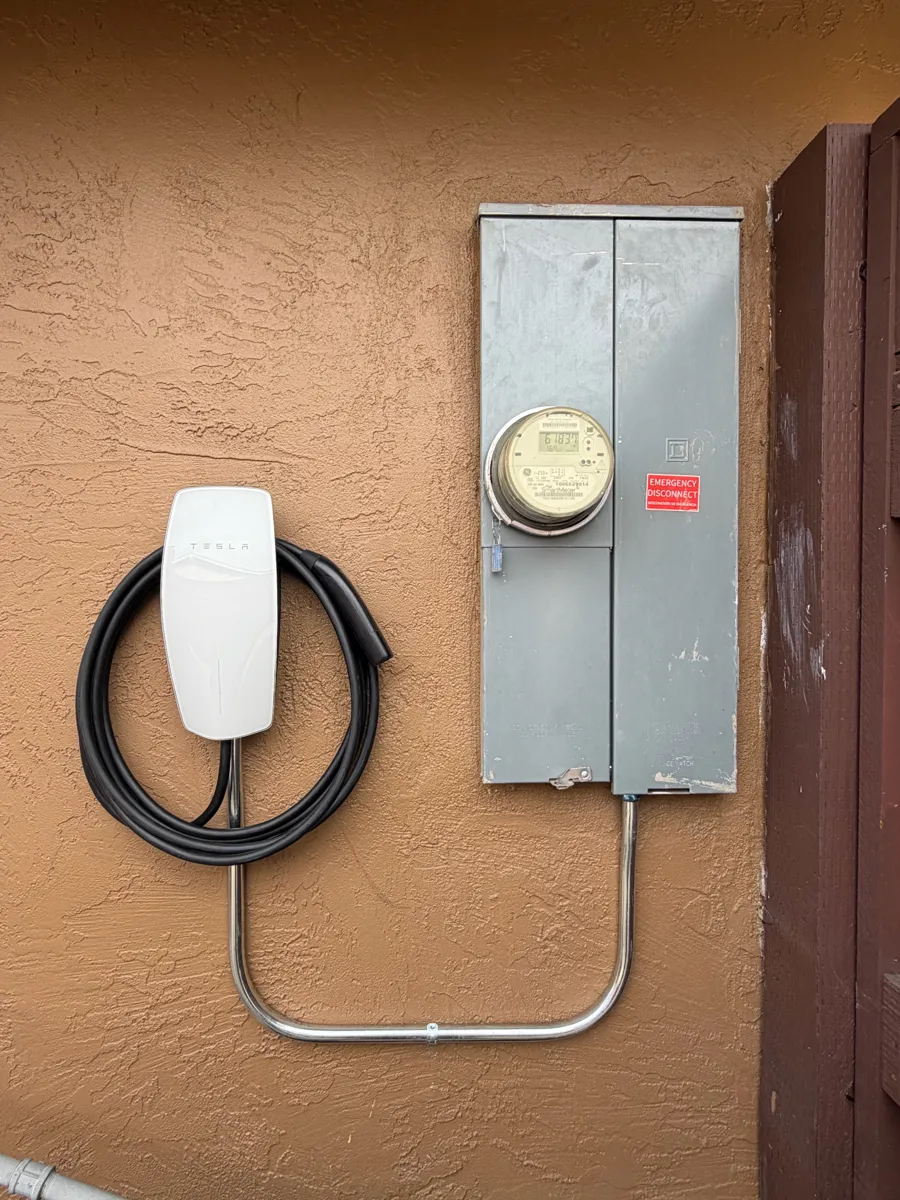 Outdoor Tesla Wall Connector next to a meter panel on a stucco wall with a clean conduit loop